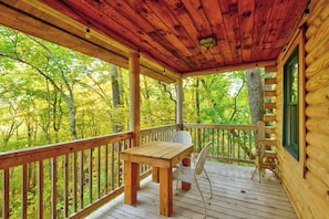 A wooden deck with a table and chairs, surrounded by a railing, overlooking a forested area. - Hideaway Homestead (Banner Elk)
