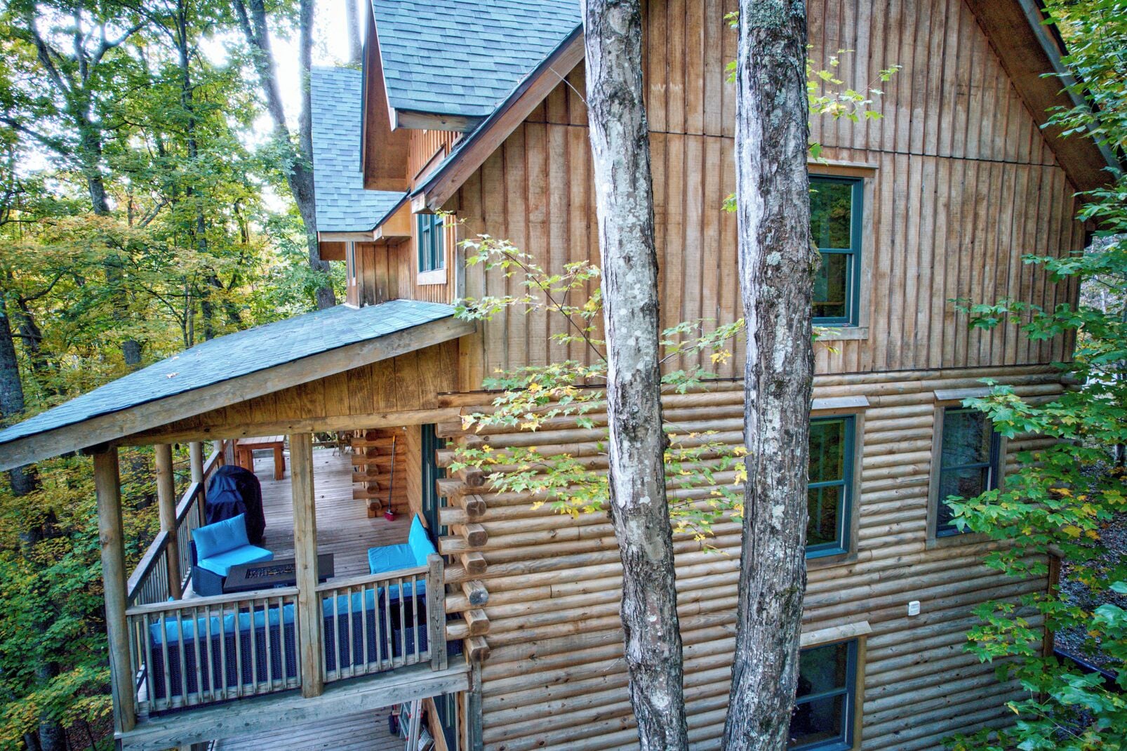 A log cabin with a porch and a deck, surrounded by trees.