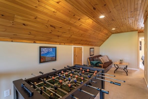 A room with a foosball table, a sofa, a small table with a plant, and a painting on the wall. - 4 Bears Lodge (Banner Elk)