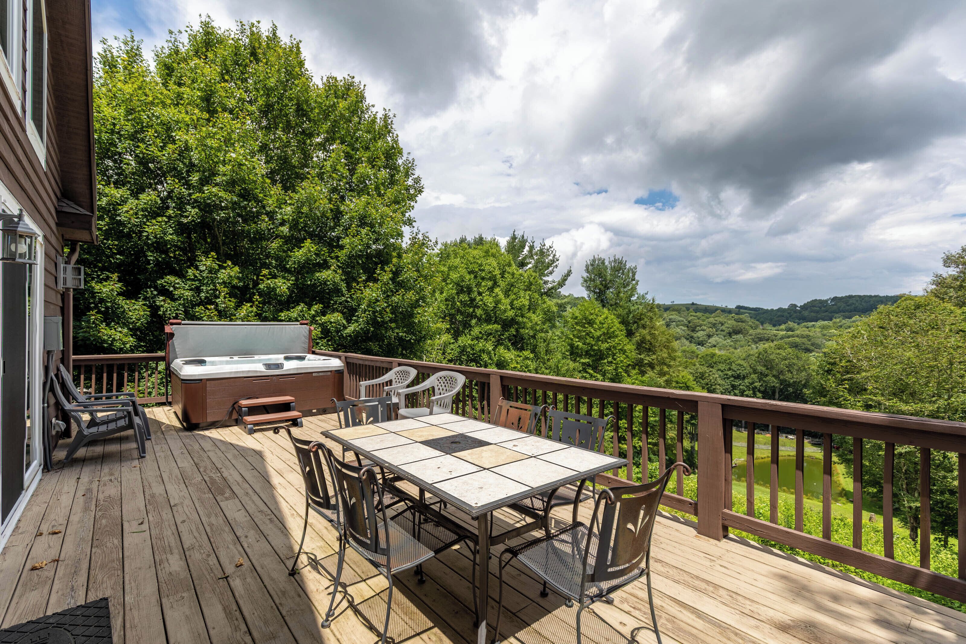 Eine Holzterrasse mit Tisch und Stühlen, einem Whirlpool und Blick auf einen bewaldeten Bereich.