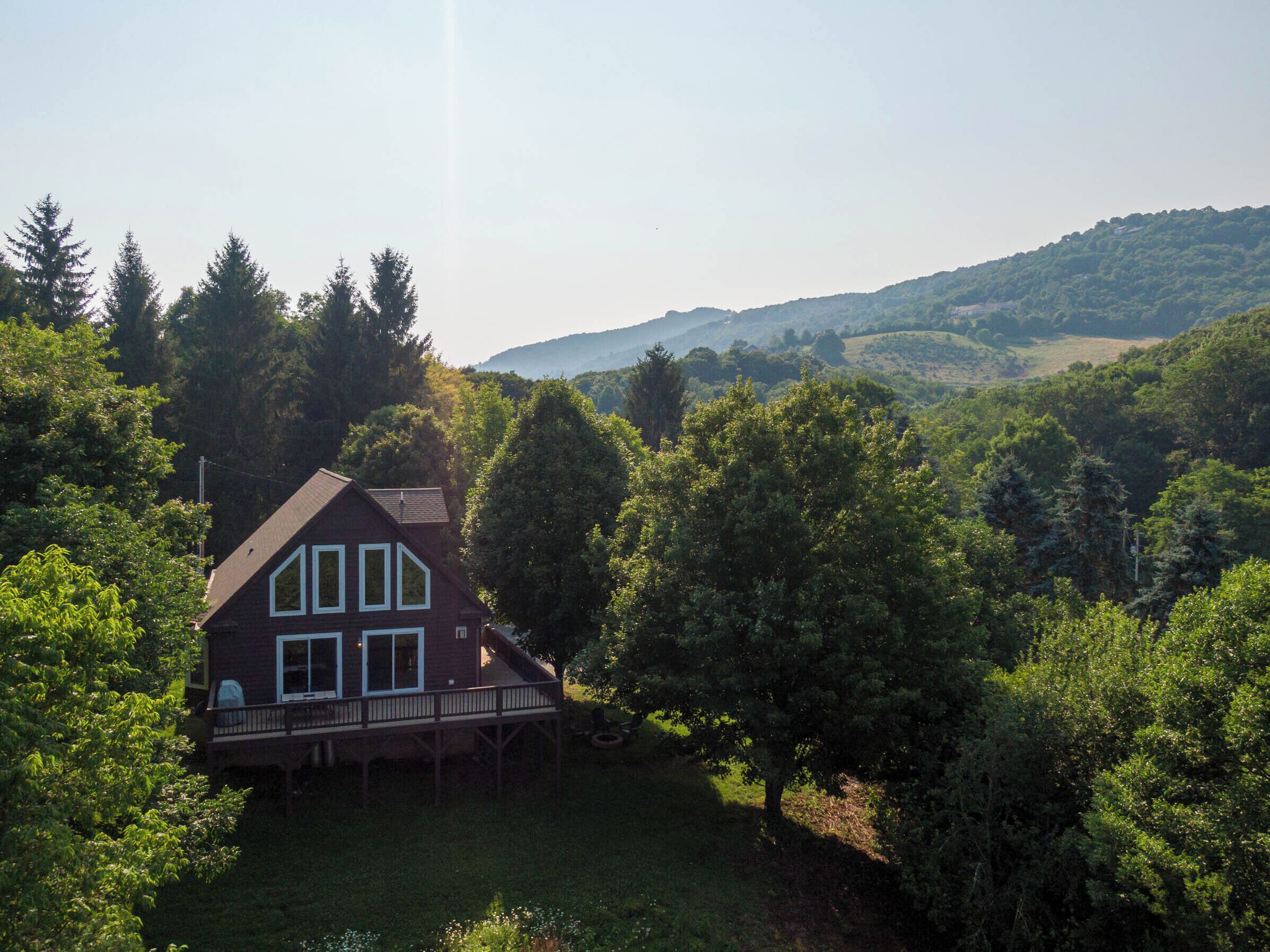 Una casa a due piani con una terrazza in legno, circondata da vegetazione lussureggiante e colline sullo sfondo.