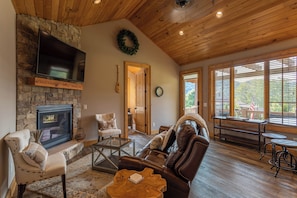 A cozy living room with a stone fireplace, leather sofa, and a television mounted on the wall. - Valley View (Banner Elk)