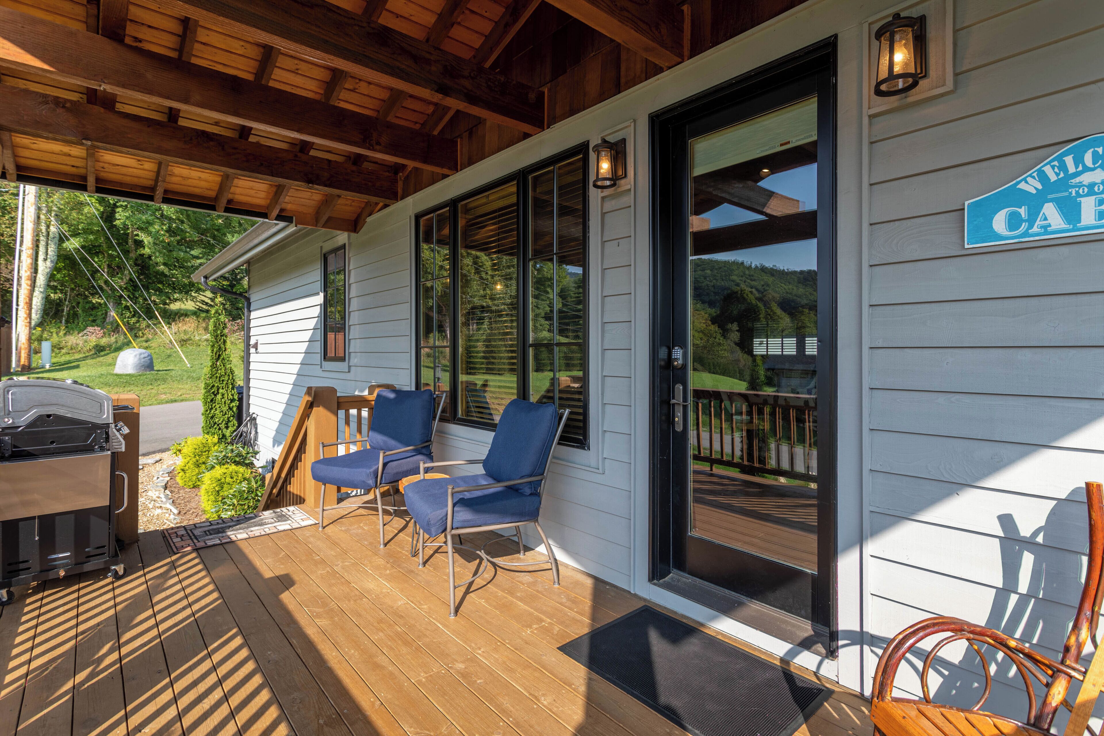 A covered porch with two blue chairs, a grill, and a welcome sign.
