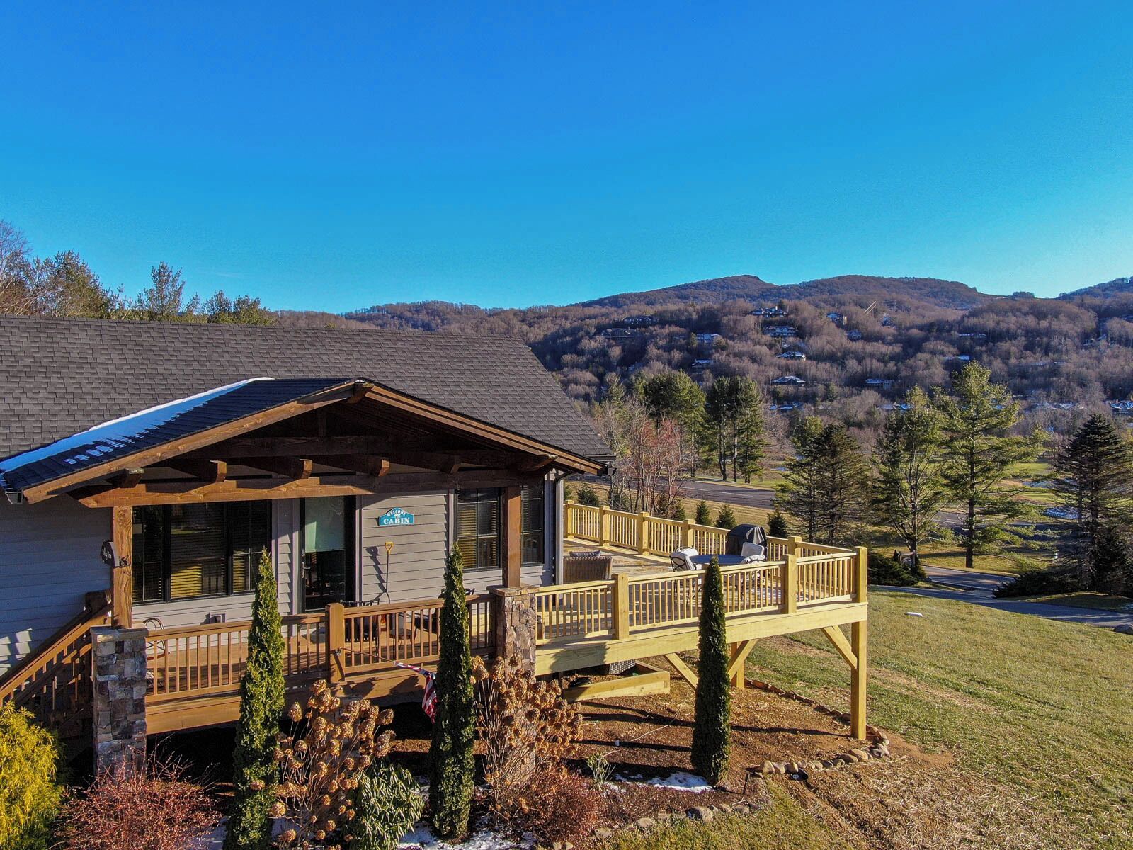 A cabin with a covered porch, a deck, and a view of the surrounding mountains.