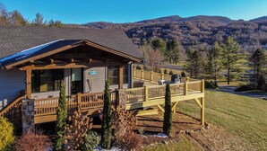 A cabin with a covered porch, a deck, and a view of the surrounding mountains. - Valley View (Banner Elk)