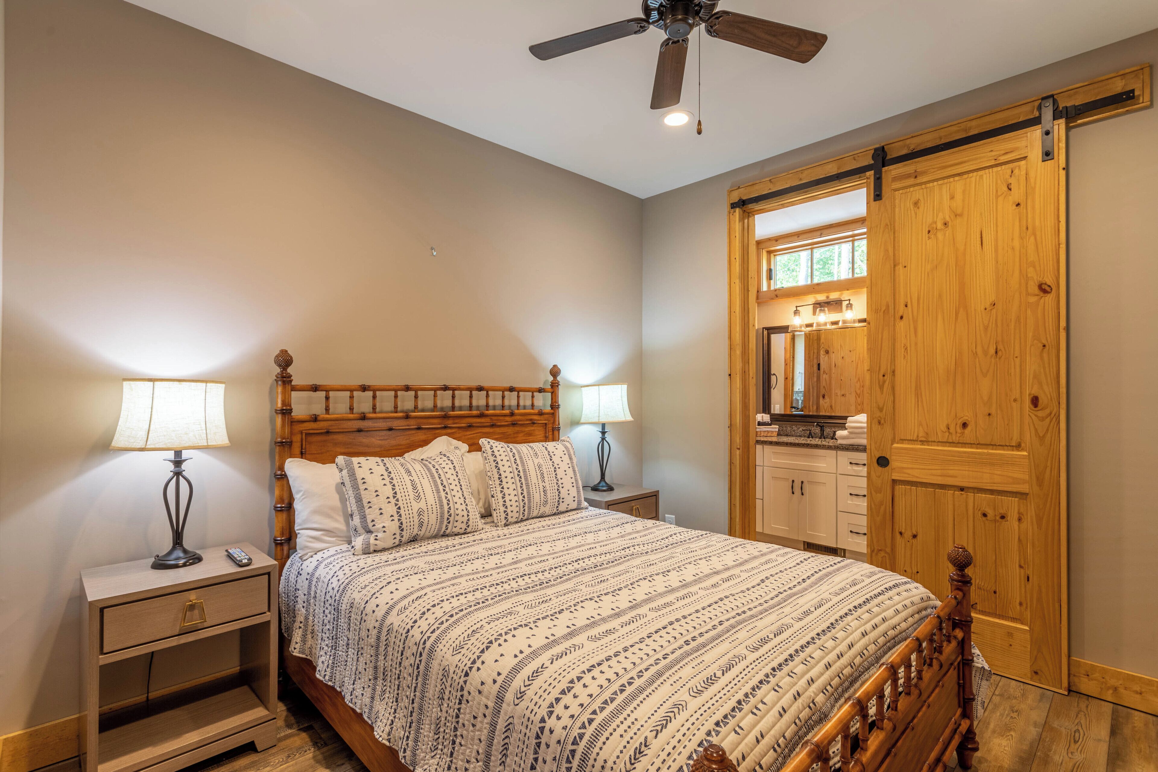 Une chambre à coucher avec un lit en bois, deux tables de chevet avec des lampes, un ventilateur de plafond et une porte coulissante en bois.