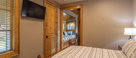 Une chambre à coucher avec un lit, des portes en bois, un ventilateur de plafond, une télévision et une fenêtre avec des stores.