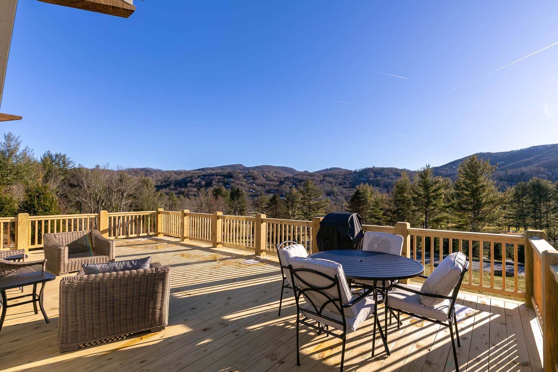 A wooden deck with outdoor furniture, a grill, and a view of a mountainous landscape.