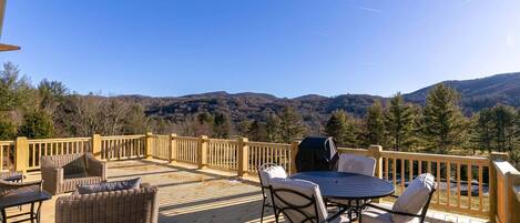 A wooden deck with outdoor furniture, a grill, and a view of a mountainous landscape.
