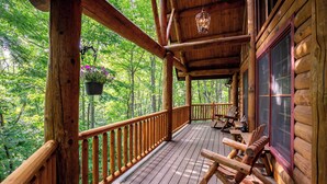 A wooden deck with a railing, a hanging light fixture, and a view of a forested area. - 4BR Running Waters Lodge at Eagles Nest (Banner Elk)