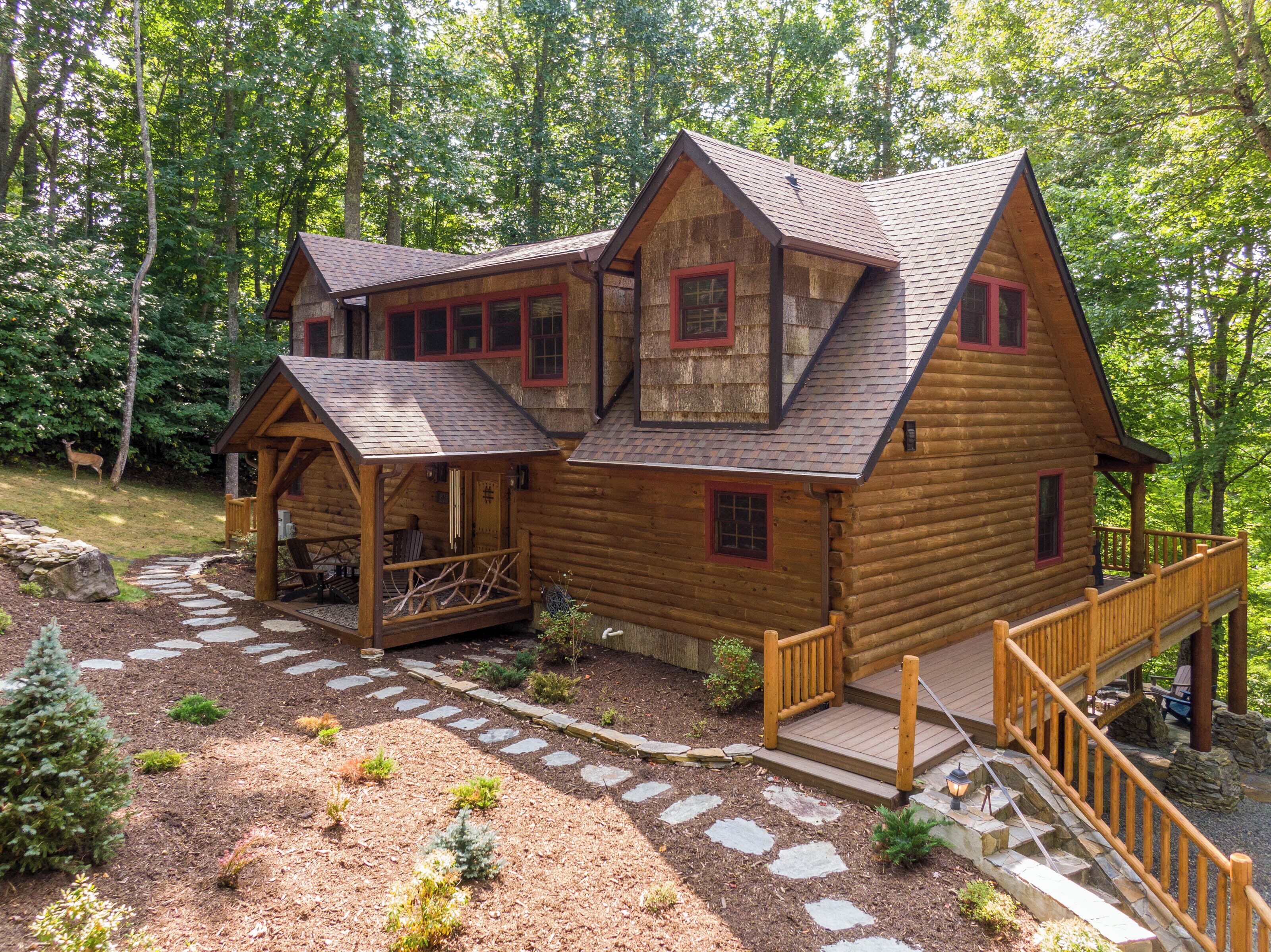 Une cabane en rondins à deux étages, dotée d’un porche et d’un chemin de pierre menant à l’entrée.