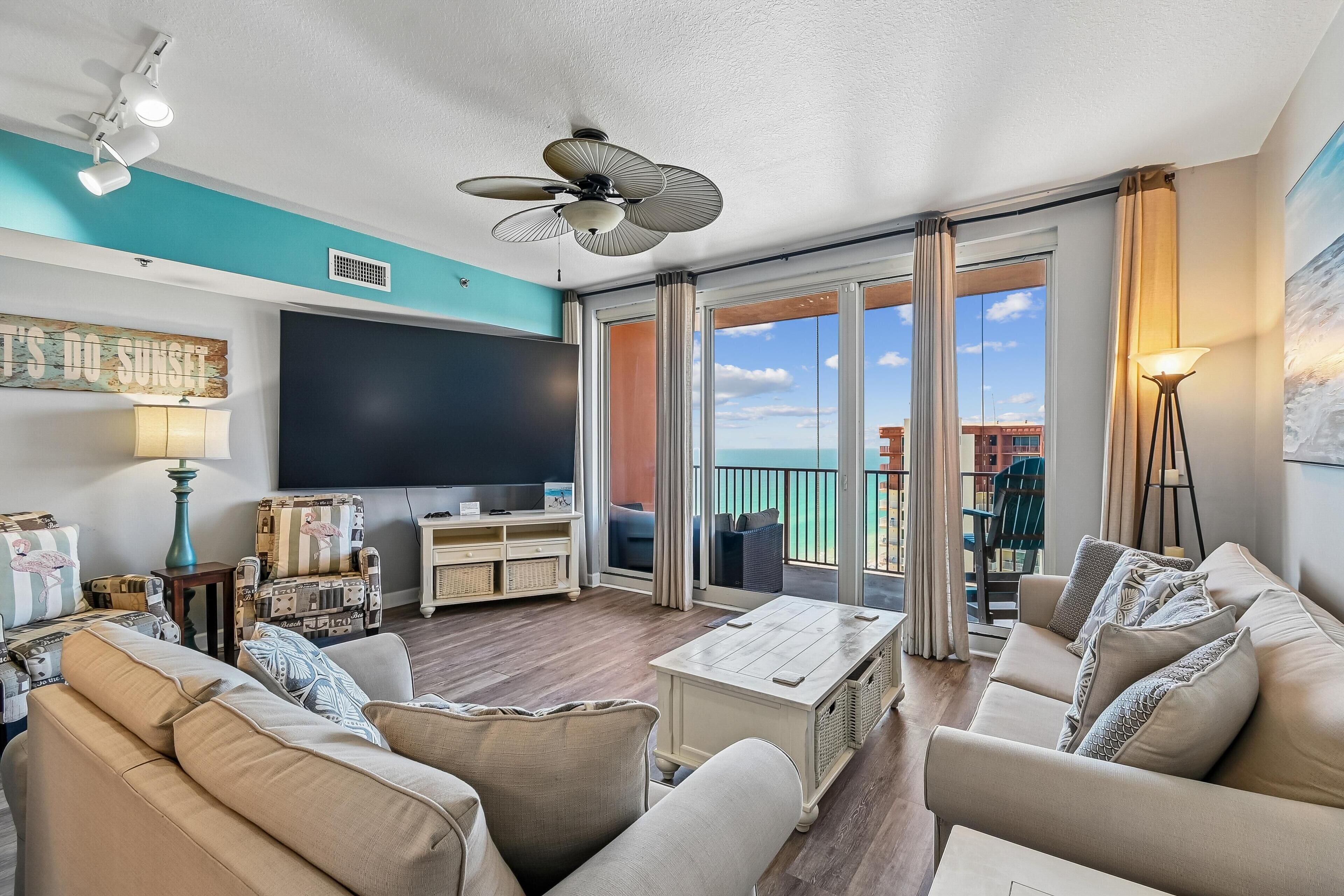 A living room with a flat-screen TV, sofas, a coffee table, and a balcony with a view.