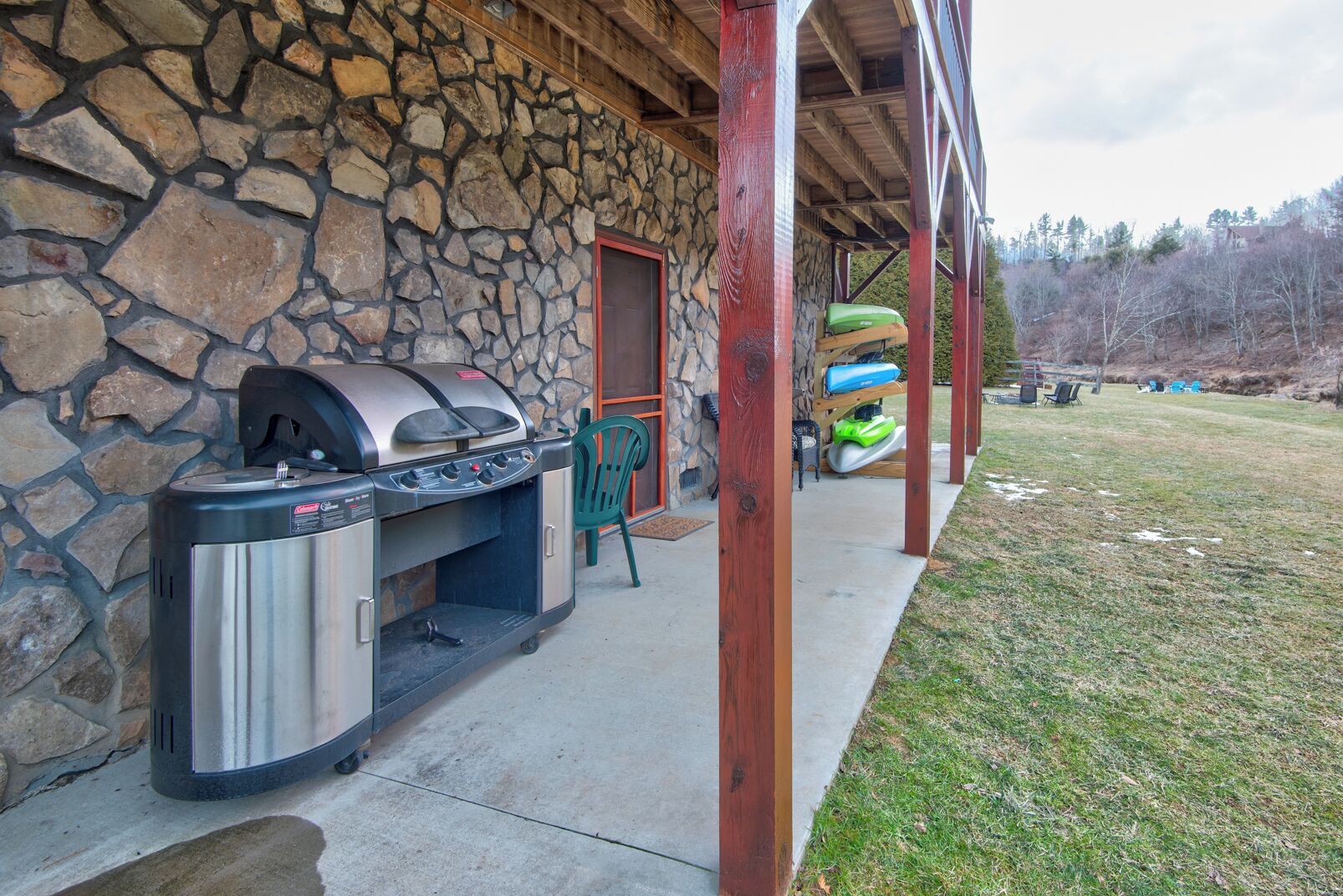 A stone exterior wall with a grill and a covered porch area.