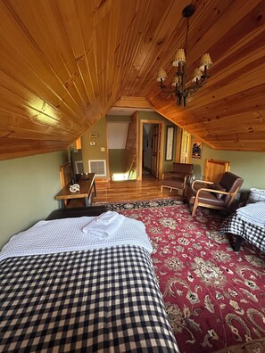 A cozy attic bedroom with two beds, a wooden ceiling, and a view of the living area. - River Roost (Todd)