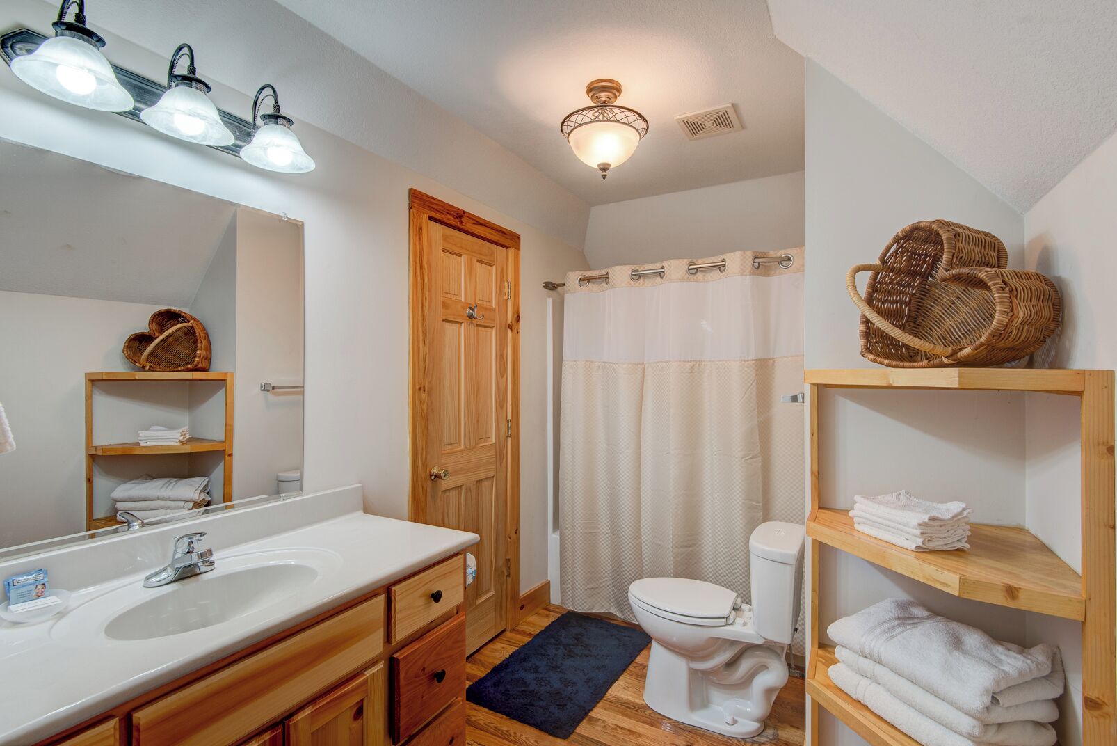 A bathroom with a wooden vanity, a large mirror, a white sink, a toilet, and a shower curtain.