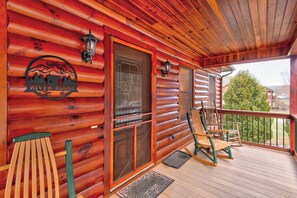 A wooden cabin with a porch, a welcome mat, and two rocking chairs. - River Roost (Todd)