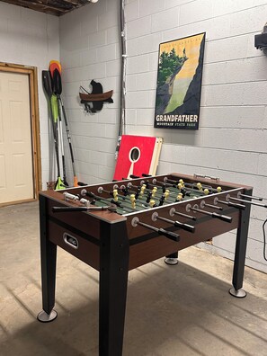 A foosball table in a room with a white brick wall, a poster of North Carolina's Grandfather Mountain, and fishing rods. - River Roost (Todd)
