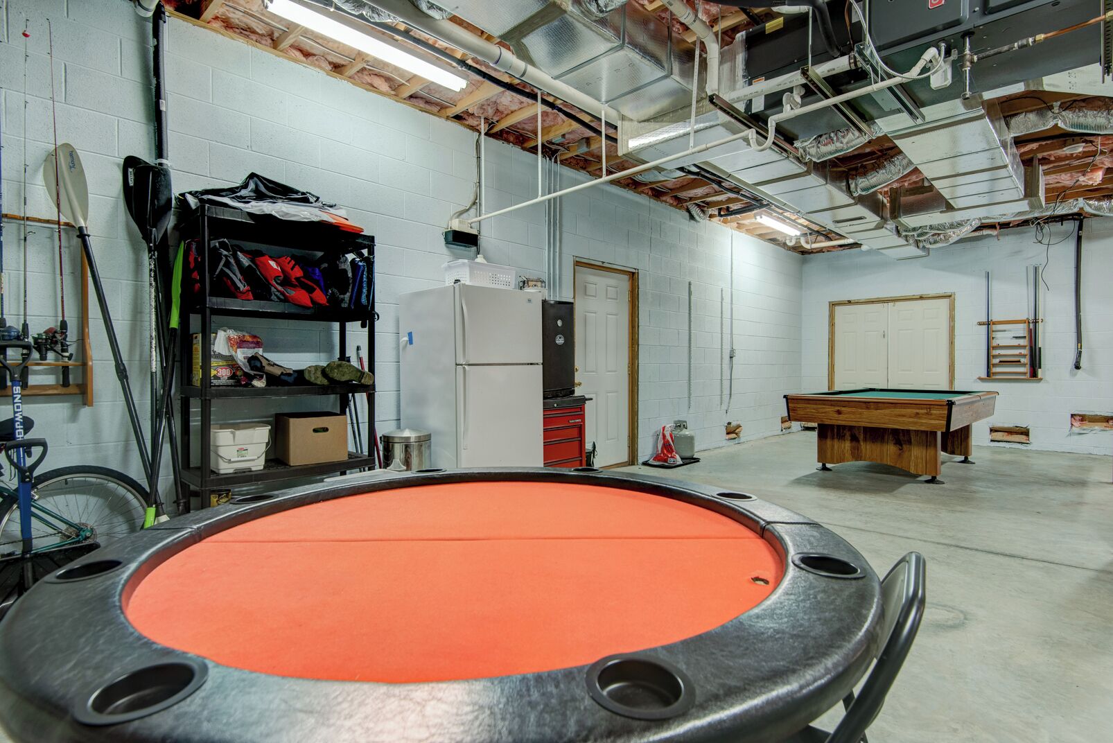 A billiards room with a pool table, a refrigerator, and a shelf with various items.