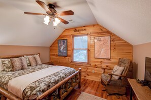 Ein Schlafzimmer mit einem Bett, einem Sessel, einem Deckenventilator und zwei Fenstern.