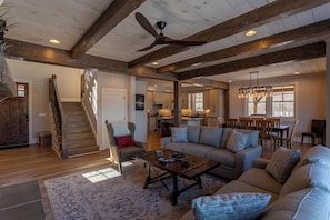 A spacious living room with a high ceiling, wooden beams, a large sofa, a coffee table, and a staircase leading to another room.