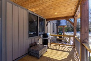 A covered deck with a grill, a wicker basket, and a small table.