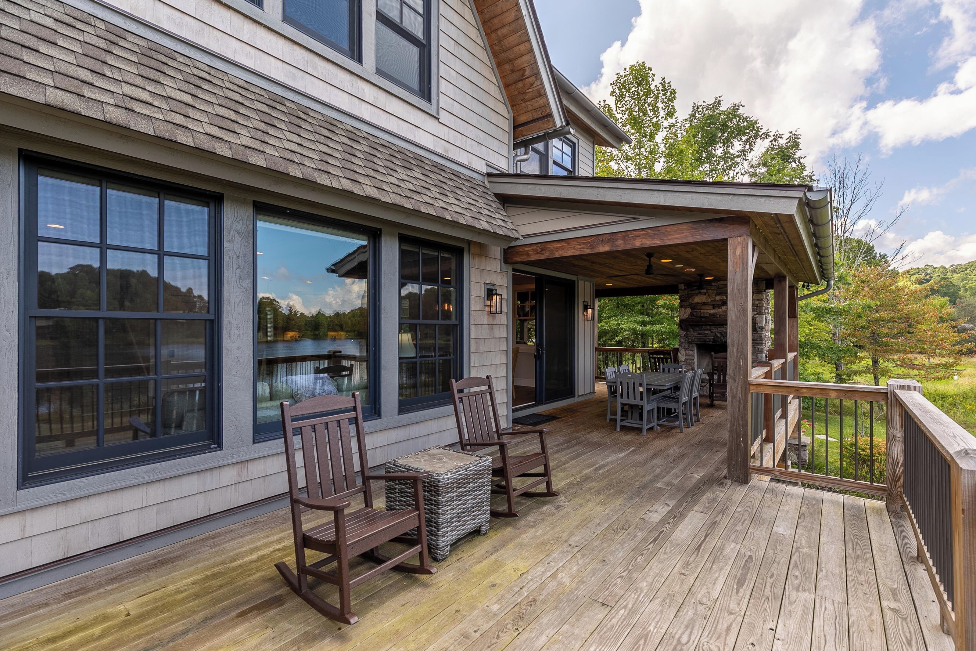 Une terrasse en bois avec des meubles d’extérieur, de grandes fenêtres et une cheminée en pierre.