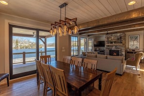 A spacious dining area with a wooden table and chairs, a cozy living room with a fireplace, and large windows offering a view of a body of water.