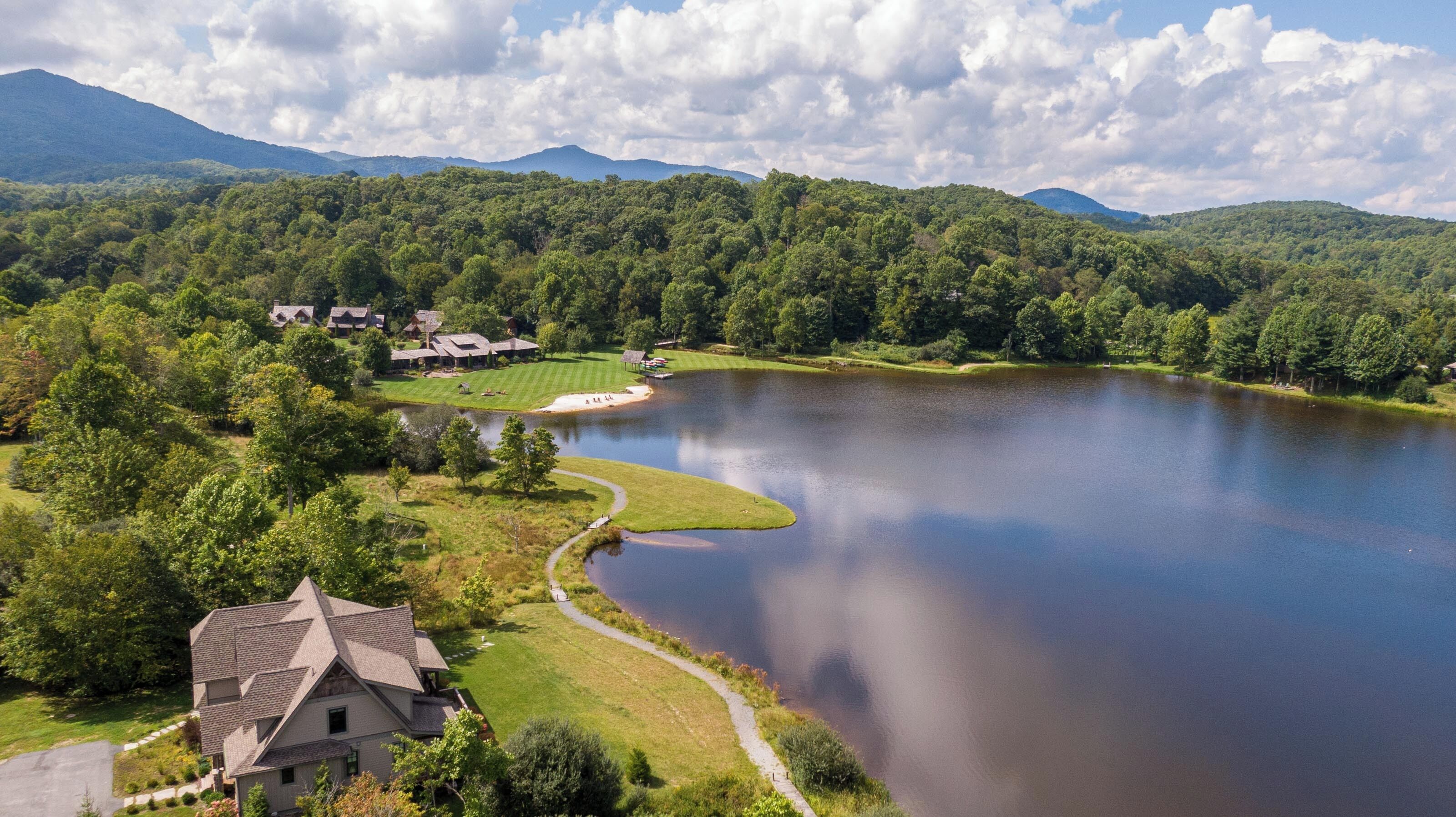 A lakeside property with a large house, a golf course, and a forested mountain backdrop.