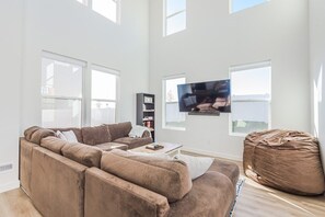 A modern living room with a large sectional sofa, a coffee table, a bean bag, and a flat-screen TV mounted on the wall. - 7773 Owens View (West Jordan)