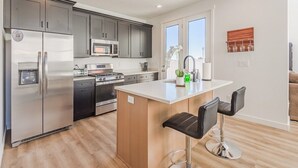 Una cocina moderna con electrodomésticos de acero inoxidable, una isla central con taburetes y vistas al exterior.
