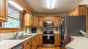A modern kitchen with wooden cabinets, stainless steel appliances, and a large window with blinds. - Nuttin' Better (Blowing Rock)