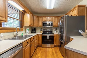 A modern kitchen with wooden cabinets, stainless steel appliances, and a large window with blinds. - Nuttin' Better (Blowing Rock)