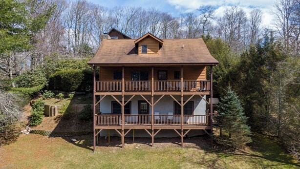 A multi-story log cabin with a balcony on each floor, surrounded by trees. - Nuttin' Better (Blowing Rock)