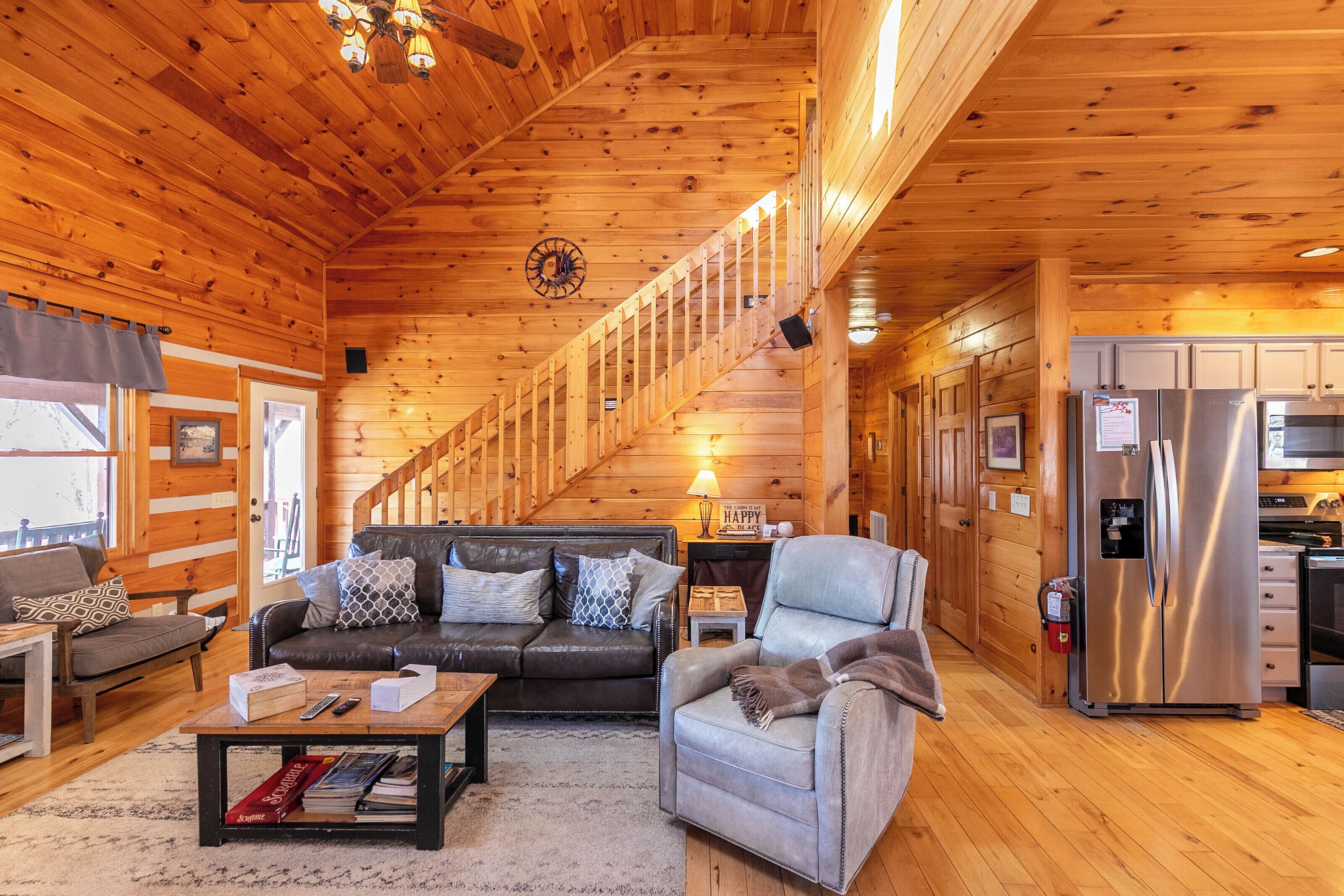 L’intérieur d’un chalet en bois comprend un salon, un canapé, un fauteuil, une table basse, une cheminée et un coin cuisine.