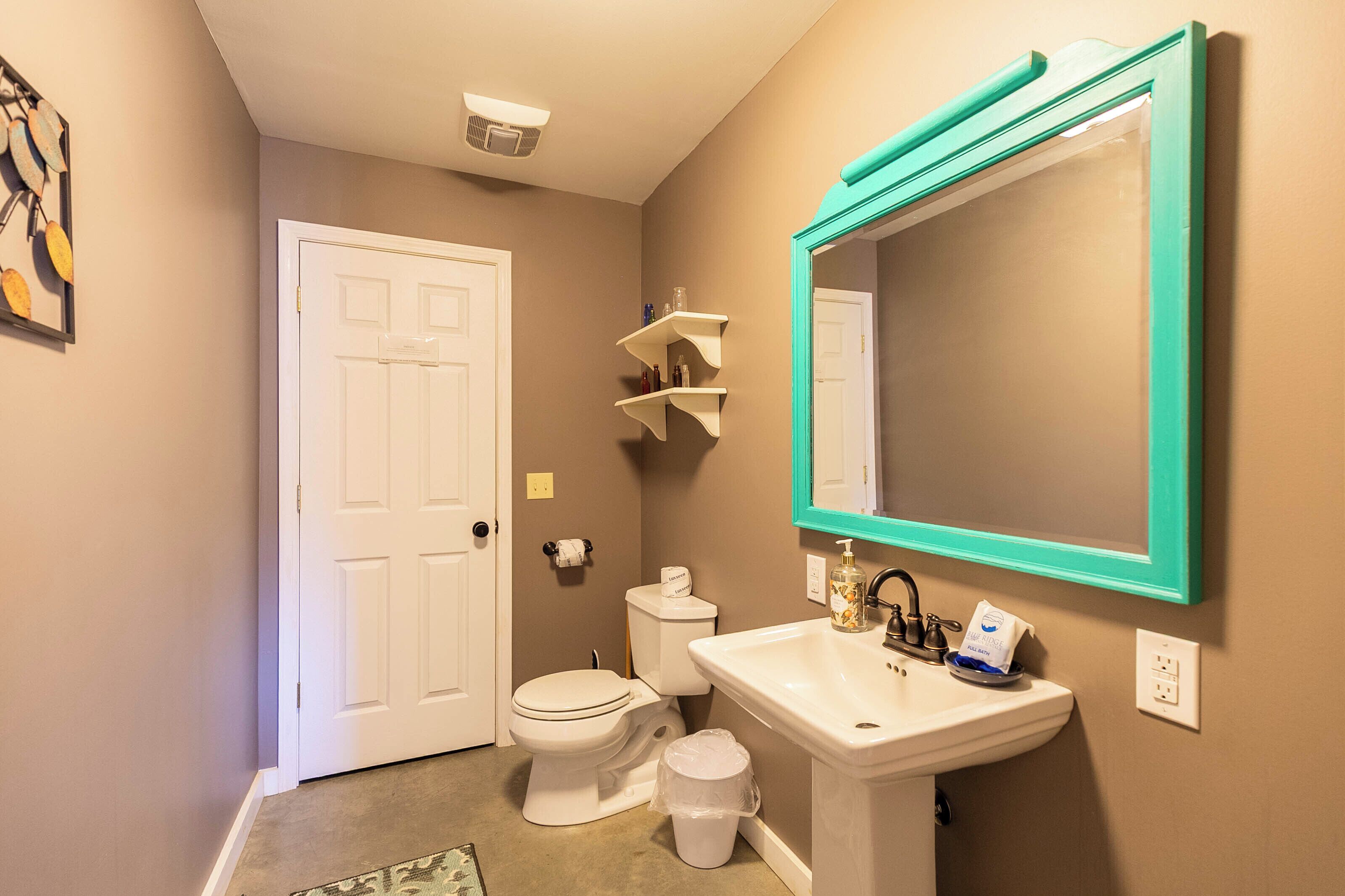 A bathroom with a toilet, sink, mirror, and shelves.