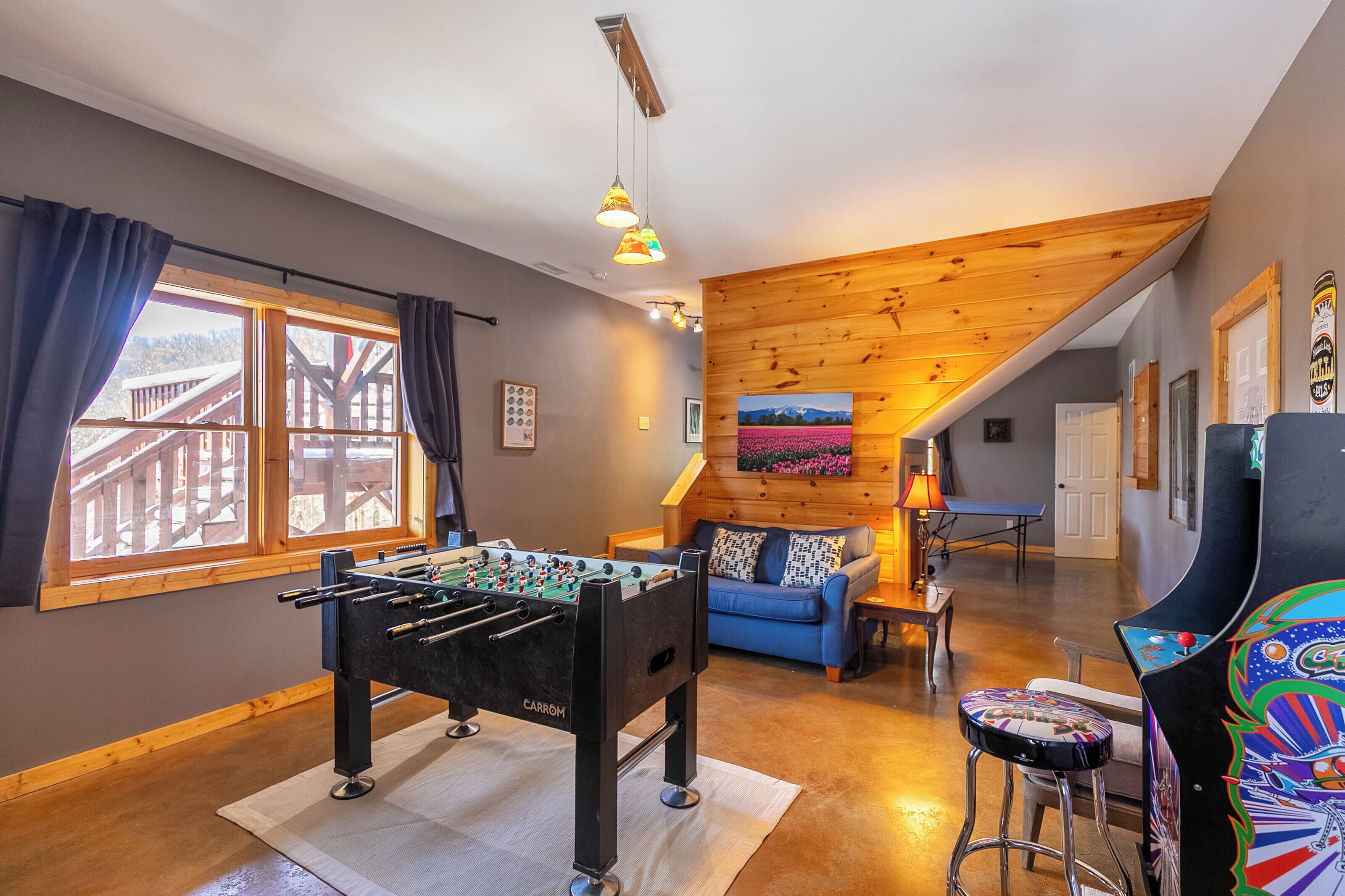 A cozy room with a foosball table, a blue sofa, and a colorful arcade machine.