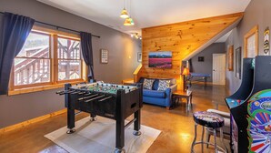 Een gezellige kamer met een tafelvoetbaltafel, een blauwe bank en een kleurrijke speelautomaat.