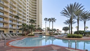 A hotel pool area with lounge chairs, palm trees, and a multi-story building with balconies. - Shores of Panama 1118 (Panama City Beach)