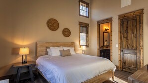 A bedroom with a wooden bed, two wall-mounted circular decorations, a nightstand with a lamp, and a wooden door. - Stillness Springs at Eagles Nest (Banner Elk)
