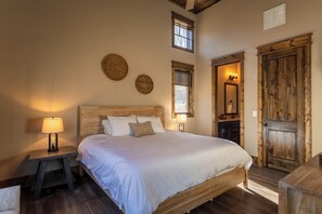 A bedroom with a wooden bed, two wall-mounted circular decorations, a nightstand with a lamp, and a wooden door. - Stillness Springs at Eagles Nest (Banner Elk)