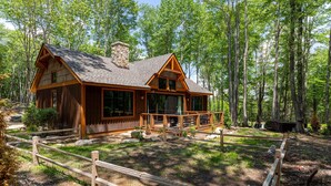 A cabin with a large porch, surrounded by a wooden fence, set in a forest. - Stillness Springs at Eagles Nest (Banner Elk)