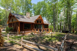 A cabin with a large porch, surrounded by a wooden fence, set in a forest. - Stillness Springs at Eagles Nest (Banner Elk)
