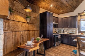 A rustic kitchen with dark wooden cabinets, a wooden bench, and a dining table set with plates and glasses. - Stillness Springs at Eagles Nest (Banner Elk)