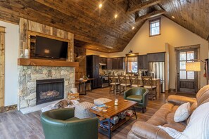 A spacious living room with a stone fireplace, wooden ceiling, and a dining area with a high table and chairs. - Stillness Springs at Eagles Nest (Banner Elk)