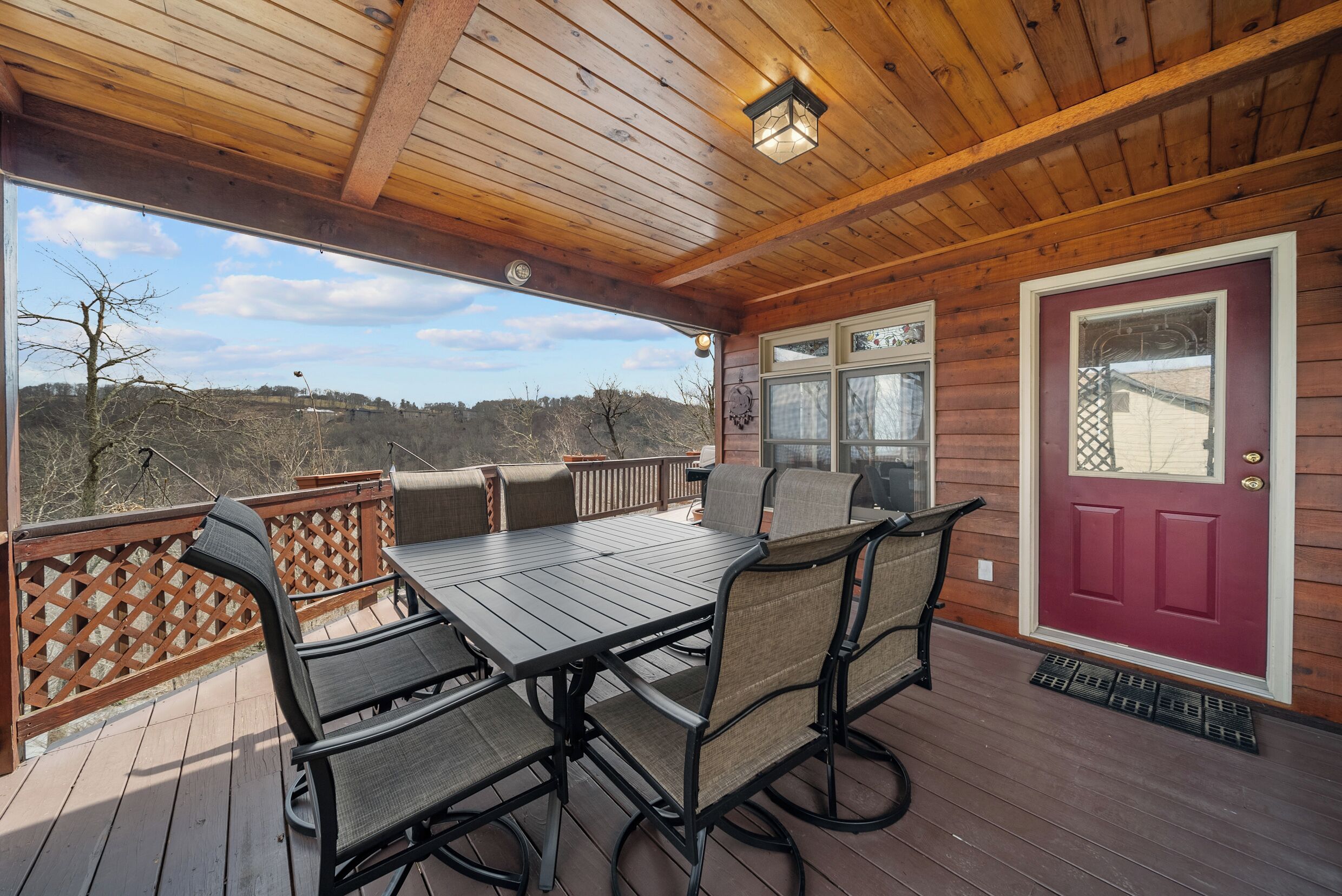A wooden deck with a table and chairs, a red door, and a view of the landscape.