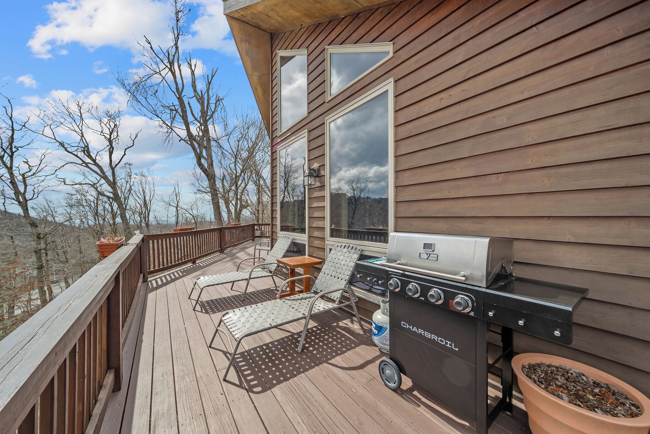 A deck with a grill, lounge chairs, and a potted plant.