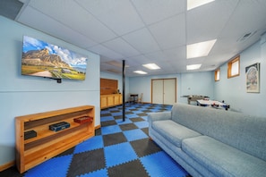 A room with a checkered floor, a sofa, a television, a wooden shelf, and a kitchen area. - Mountain Sunrise (Banner Elk)