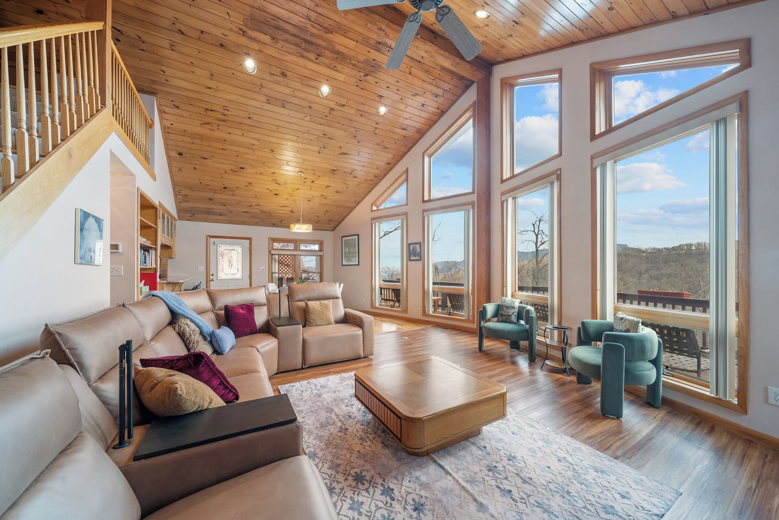 A spacious living room with a high ceiling, large windows, and a wooden staircase.