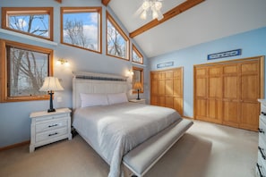 A bedroom with a bed, bedside tables, a bench, wooden wardrobe, and large windows. - Mountain Sunrise (Banner Elk)