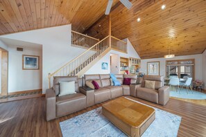 A spacious living area with a wooden ceiling, a brown leather sofa, a wooden coffee table, and a staircase leading to an upper level. - Mountain Sunrise (Banner Elk)